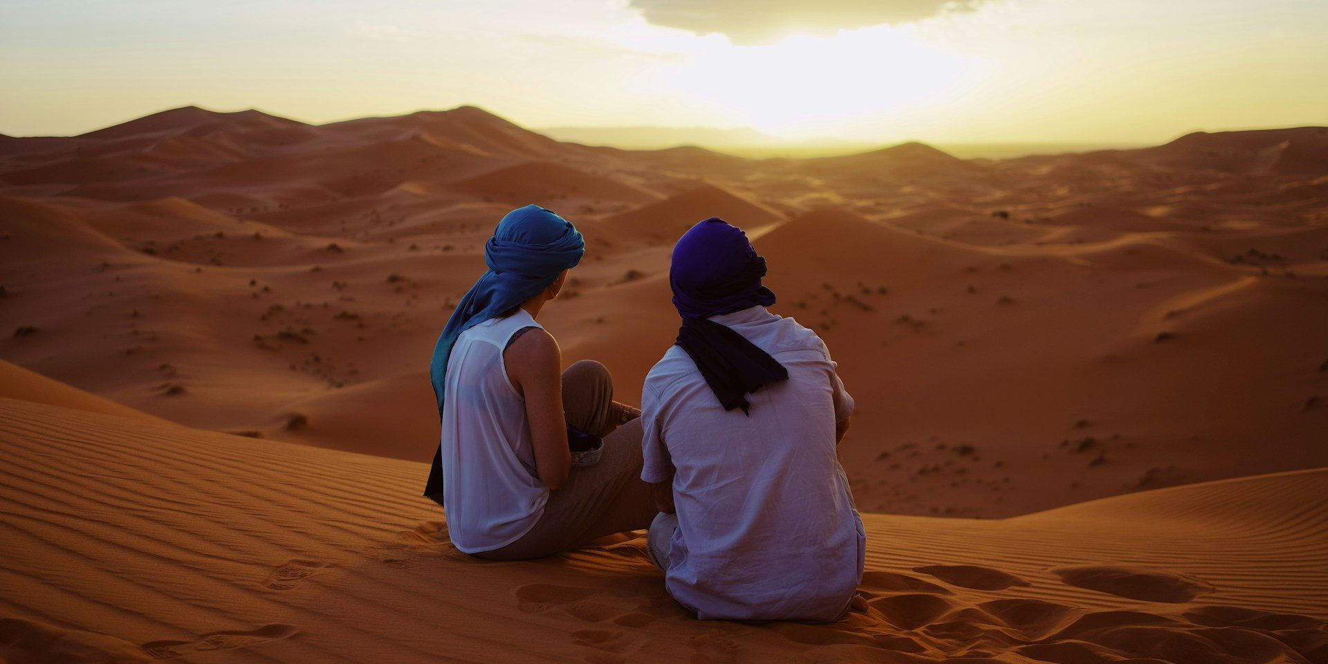 Couples setting in the top of a dune in the Sahara desert observing the sunset
